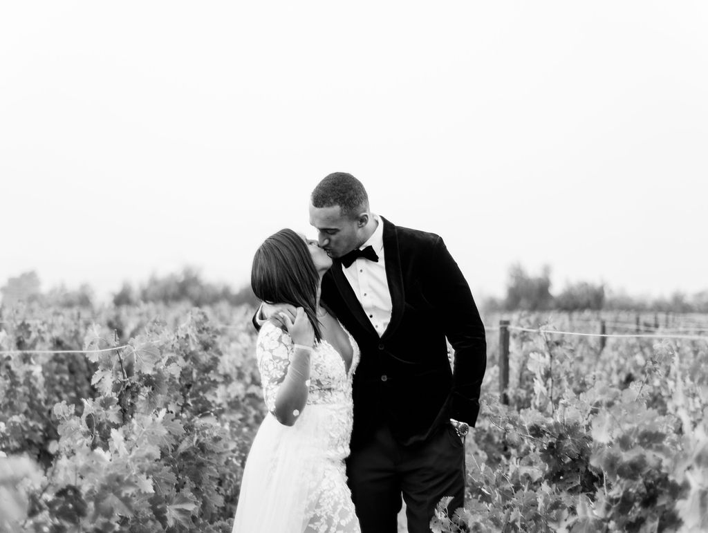 black and white photo of bride and groom kissing in a vineyard